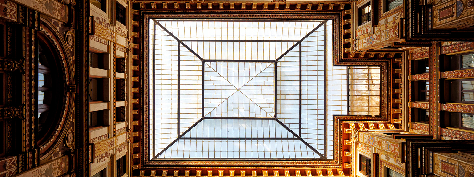 Yard in the Sciarra Galery in central Rome, close to the Fontana di Trevi. This image is taken from the ground level looking up towards the glass ceiling, with the colourful art deco walls in all four sides of the image. Image taken on a very sunny winter afternoon.